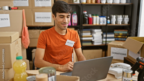 Smiling young hispanic man volunteering at local charity center, sitting with laptop on table