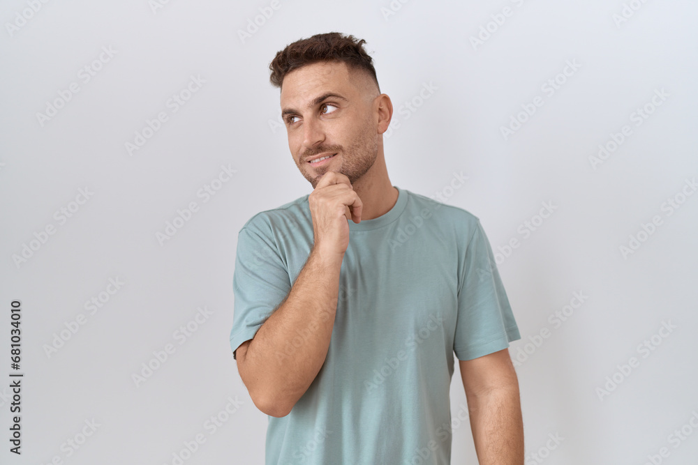 Hispanic man with beard standing over white background with hand on chin thinking about question, pensive expression. smiling and thoughtful face. doubt concept. Hispanic man with beard standing over white background with hand on chin thinking about question, pensive expression. smiling and thoughtful face. doubt concept.