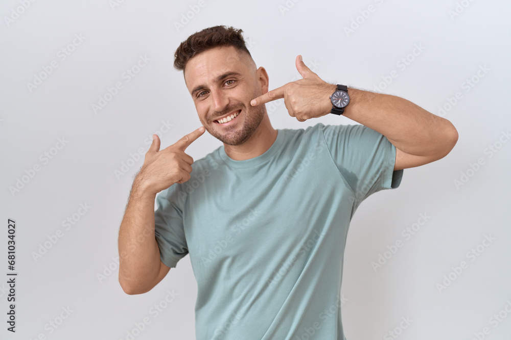 Hispanic man with beard standing over white background smiling cheerful showing and pointing with fingers teeth and mouth. dental health concept. Hispanic man with beard standing over white background smiling cheerful showing and pointing with fingers teeth and mouth. dental health concept.