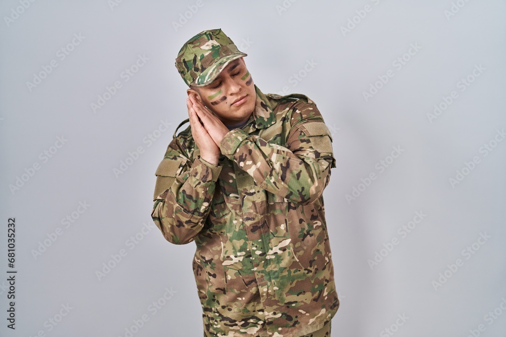 Hispanic young man wearing camouflage army uniform sleeping tired dreaming and posing with hands together while smiling with closed eyes. Hispanic young man wearing camouflage army uniform sleeping tired dreaming and posing with hands together while smiling with closed eyes.