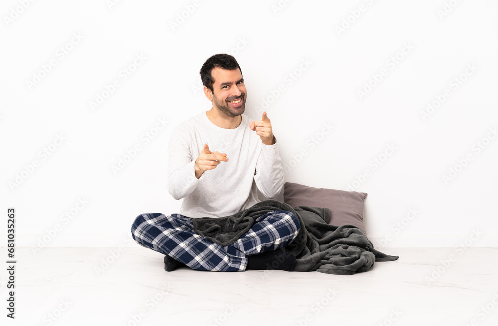 Caucasian man in pajamas sitting on the floor at indoors pointing front with happy expression
