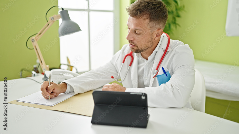 Young man doctor using touchpad writing medical report at clinic