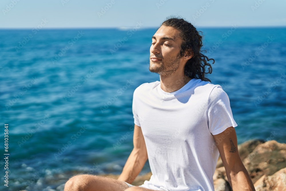 Fototapeta premium Young hispanic man breathing with closed eyes at seaside