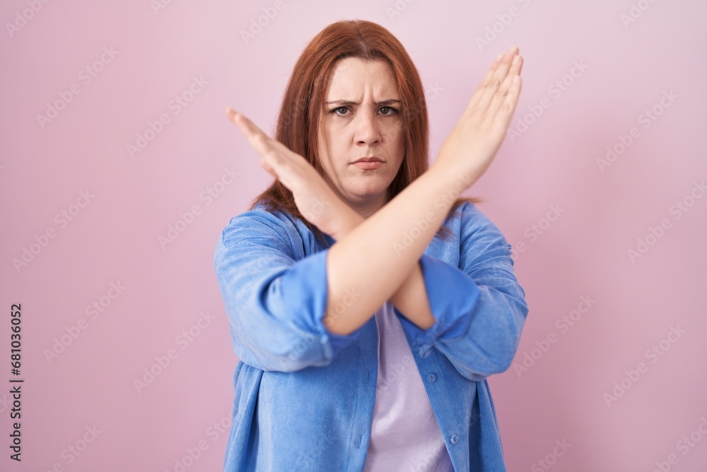 Young hispanic woman with red hair standing over pink background rejection expression crossing arms doing negative sign, angry face Young hispanic woman with red hair standing over pink background rejection expression crossing arms doing negative sign, angry face
