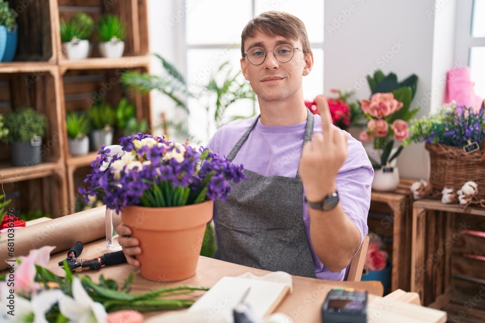 Caucasian blond man working at florist shop showing middle finger, impolite and rude fuck off expression