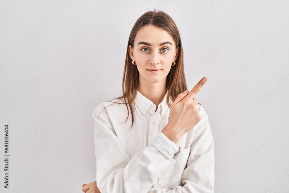 Young caucasian woman standing over isolated background pointing with hand finger to the side showing advertisement, serious and calm face