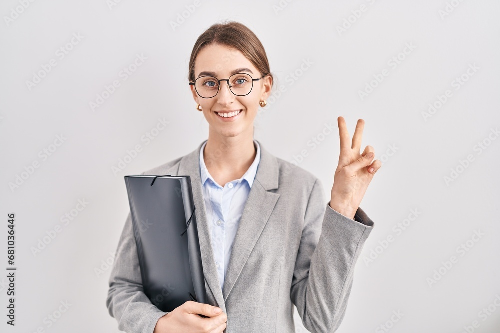 Young caucasian woman wearing business clothes and glasses smiling with happy face winking at the camera doing victory sign with fingers. number two. Young caucasian woman wearing business clothes and glasses smiling with happy face winking at the camera doing victory sign with fingers. number two.