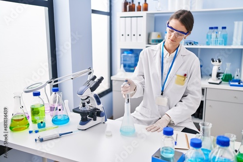 Young caucasian woman scientist pouring liquid on test tube at laboratory