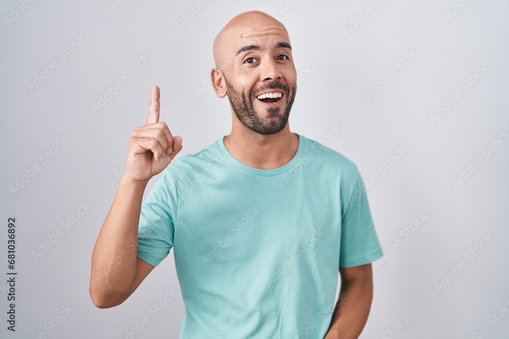 Middle age bald man standing over white background pointing finger up with successful idea. exited and happy. number one. Middle age bald man standing over white background pointing finger up with successful idea. exited and happy. number one.