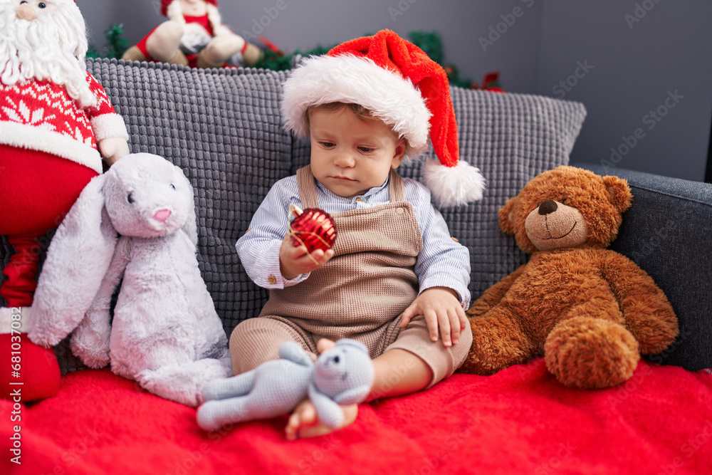 Adorable blond toddler sitting on sofa wearing christmas hat at home