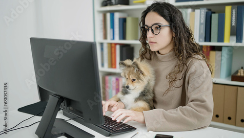 Young hispanic woman with dog student using computer studying at library university photo