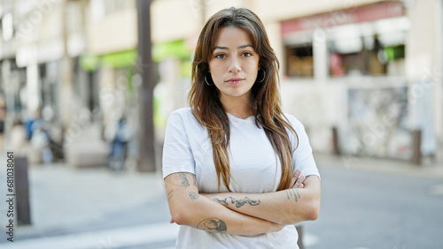 Young beautiful hispanic woman standing with serious expression with arms crossed gesture at street photo