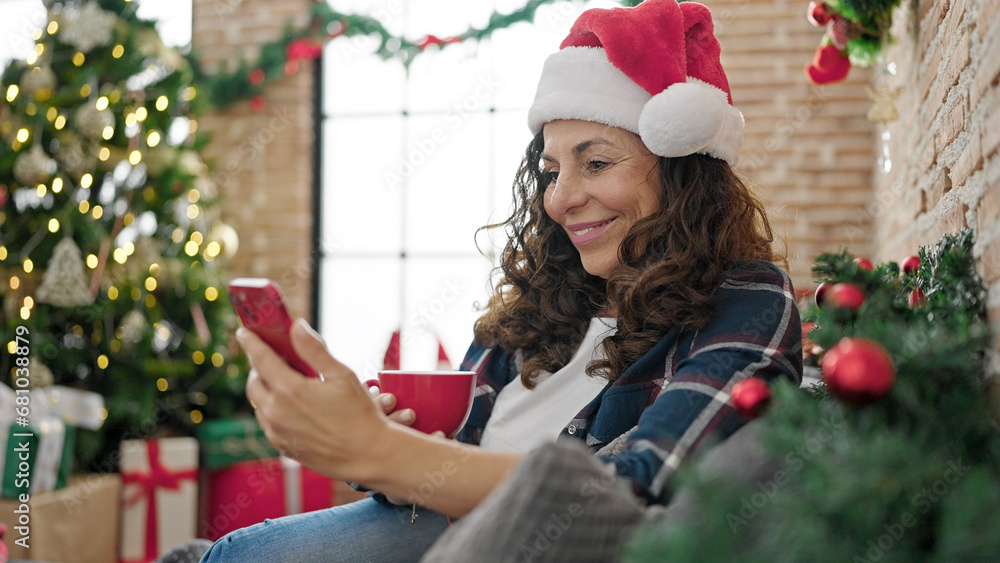 Middle age hispanic woman using smartphone drinking coffee celebrating christmas at home Middle age hispanic woman using smartphone drinking coffee celebrating christmas at home