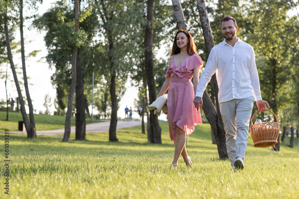 Couple holding hands while carrying picnic basket on garden background. Young family having a date at local park. Romantic relationships outdoors leisure. Husband invite his wife celebrate anniversary Couple holding hands while carrying picnic basket on garden background. Young family having a date at local park. Romantic relationships outdoors leisure. Husband invite his wife celebrate anniversary