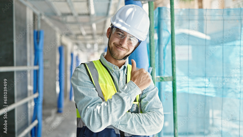 Young caucasian man architect standing with arms crossed gesture doing thumb up gesture at construction place Young caucasian man architect standing with arms crossed gesture doing thumb up gesture at construction place
