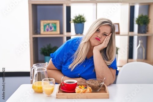 Caucasian plus size woman eating breakfast at home thinking looking tired and bored with depression problems with crossed arms.