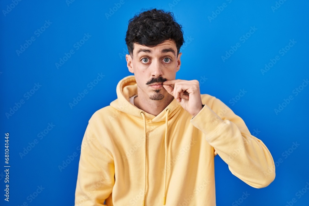 Naklejka premium Hispanic man standing over blue background mouth and lips shut as zip with fingers. secret and silent, taboo talking