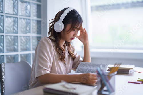 Young asian student in casual clothes wearing headphones to listening the music and reading textbook to thinking ideas while studying education knowledge and doing homework assignments in university photo
