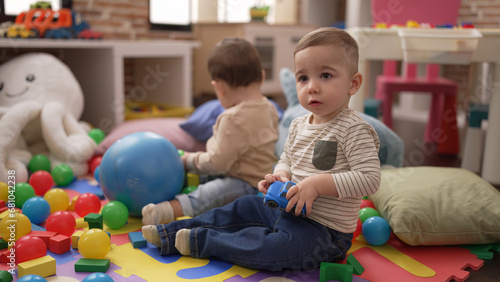Two adorable toddlers playing with balls and car sitting on floor at kindergarten