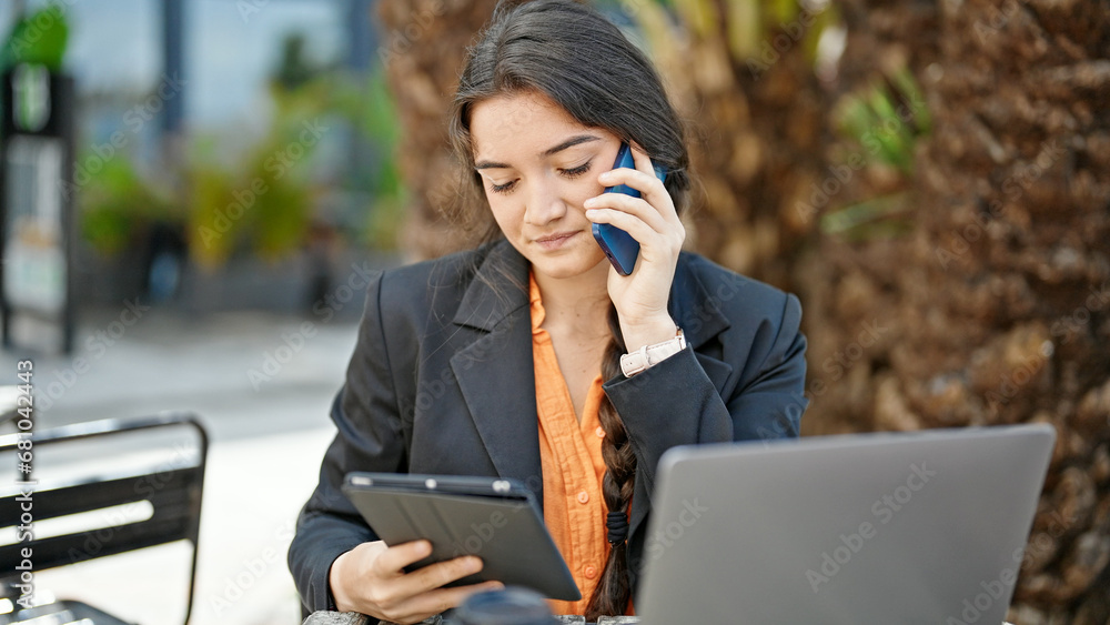 Young beautiful hispanic woman business worker talking on smartphone looking touchpad at coffee shop terrace Young beautiful hispanic woman business worker talking on smartphone looking touchpad at coffee shop terrace