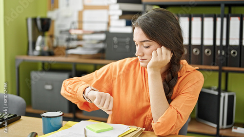 Young beautiful hispanic woman business worker looking clock with serious face at office