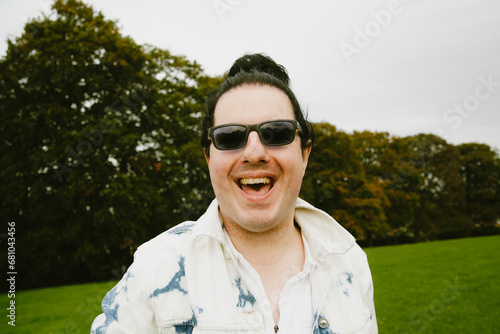 Happy guy with long hair in a bun at the park smiling into camera