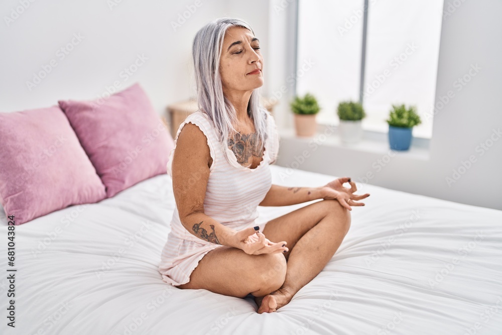 Middle age grey-haired woman doing yoga exercise sitting on bed at bedroom Middle age grey-haired woman doing yoga exercise sitting on bed at bedroom
