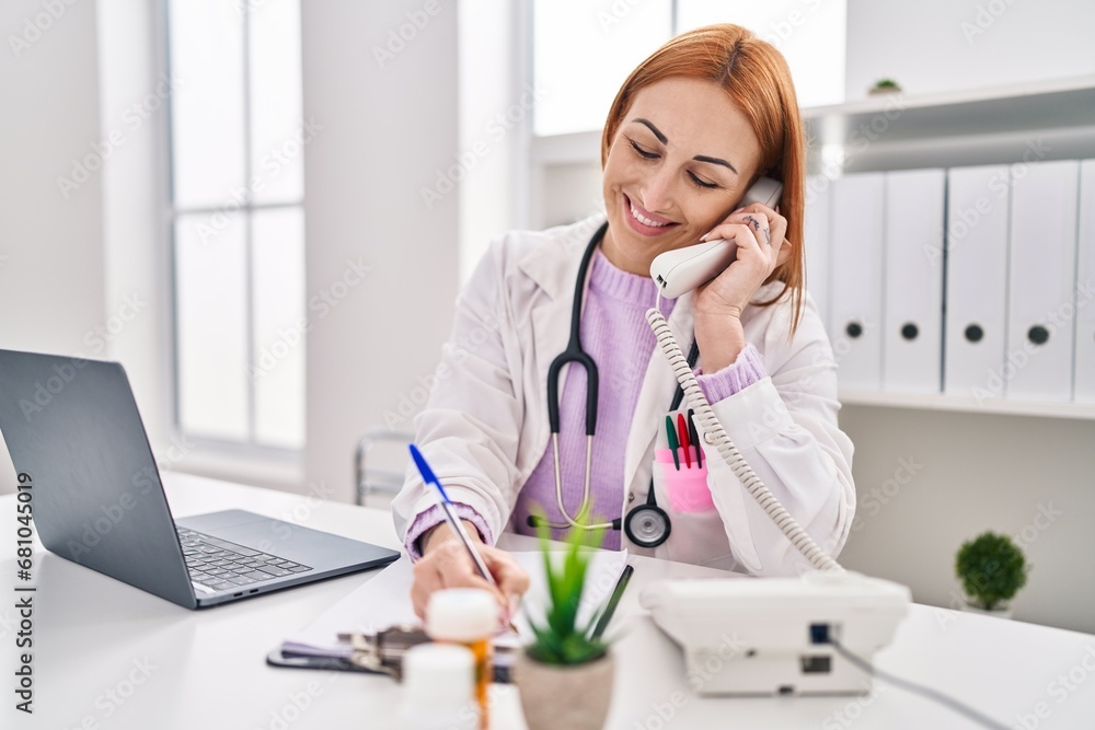Young caucasian woman doctor talking on telephone writing medical report at clinic Young caucasian woman doctor talking on telephone writing medical report at clinic