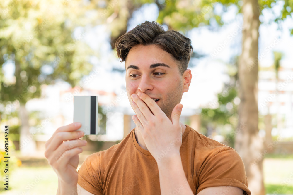Young handsome man holding a credit card with surprised expression Young handsome man holding a credit card with surprised expression