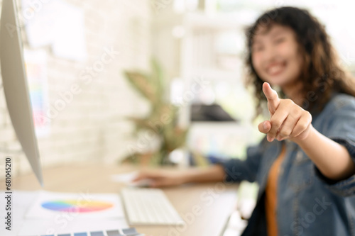 Happy blurred young woman graphic designer pointing finger at camera. Select focus to finger.