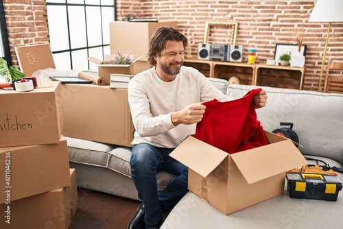 Middle age man smiling confident unpacking cardboard box at new home photo