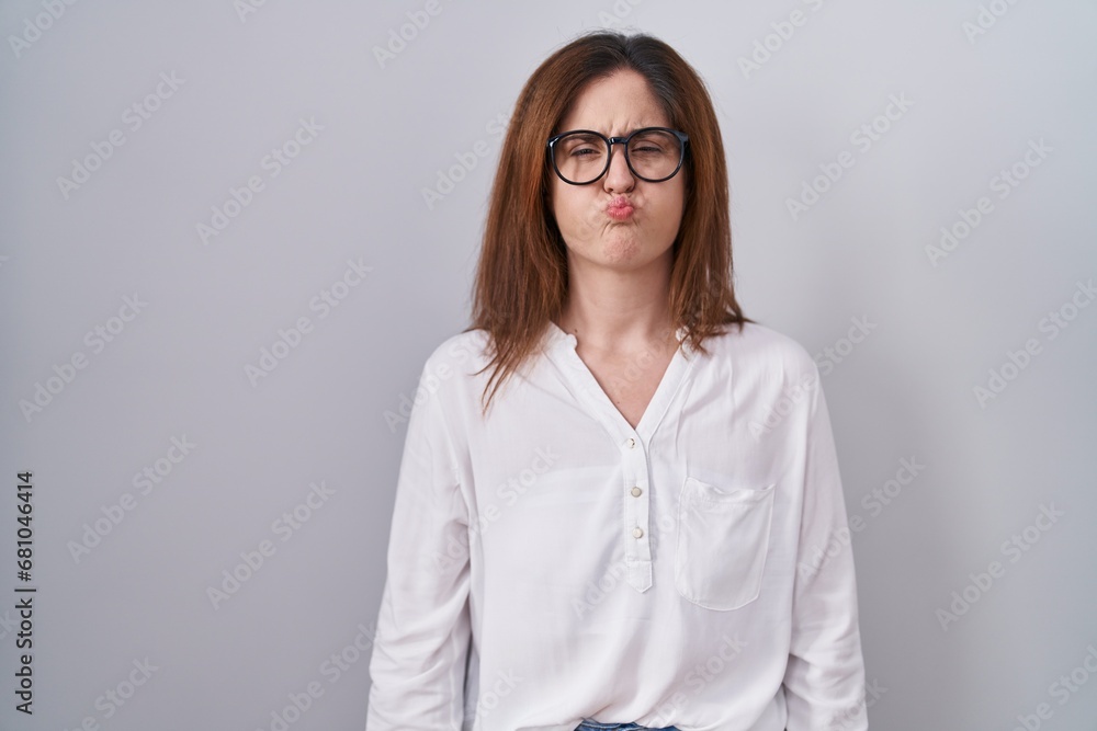 Brunette woman standing over white isolated background puffing cheeks with funny face. mouth inflated with air, crazy expression. Brunette woman standing over white isolated background puffing cheeks with funny face. mouth inflated with air, crazy expression.