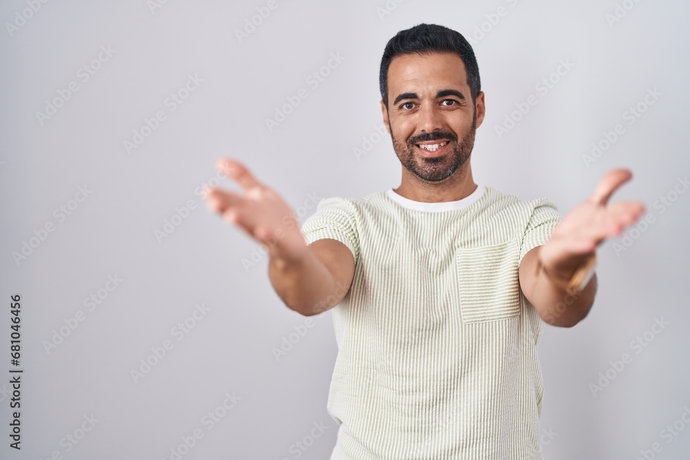 Hispanic man with beard standing over isolated background smiling cheerful offering hands giving assistance and acceptance. Hispanic man with beard standing over isolated background smiling cheerful offering hands giving assistance and acceptance.