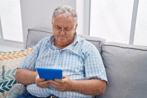 Middle age grey-haired man using touchpad sitting on sofa at home