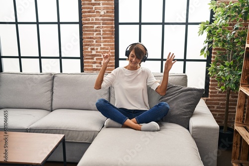 Young beautiful hispanic woman listening to music sitting on sofa dancing at home