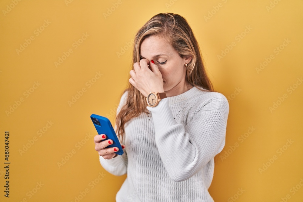 Young blonde woman using smartphone typing message tired rubbing nose and eyes feeling fatigue and headache. stress and frustration concept. - obrazy, fototapety, plakaty 