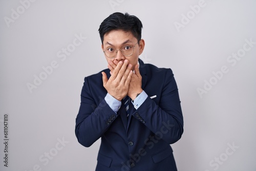 Young asian man wearing business suit and tie shocked covering mouth with hands for mistake. secret concept.