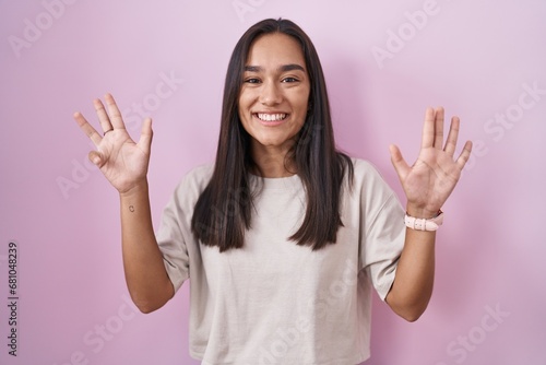 Young hispanic woman standing over pink background showing and pointing up with fingers number nine while smiling confident and happy. © Krakenimages.com
