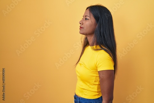 Young indian woman standing over yellow background looking to side, relax profile pose with natural face and confident smile.