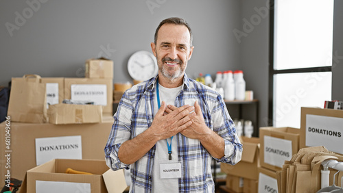 Confident grey-haired middle-aged man standing with heart filled hands, smiling as a volunteer in his community charity center © Krakenimages.com