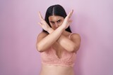 Young hispanic woman wearing pink bra rejection expression crossing arms doing negative sign, angry face