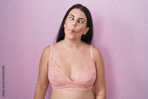 Young hispanic woman wearing pink bra making fish face with lips, crazy and comical gesture. funny expression.