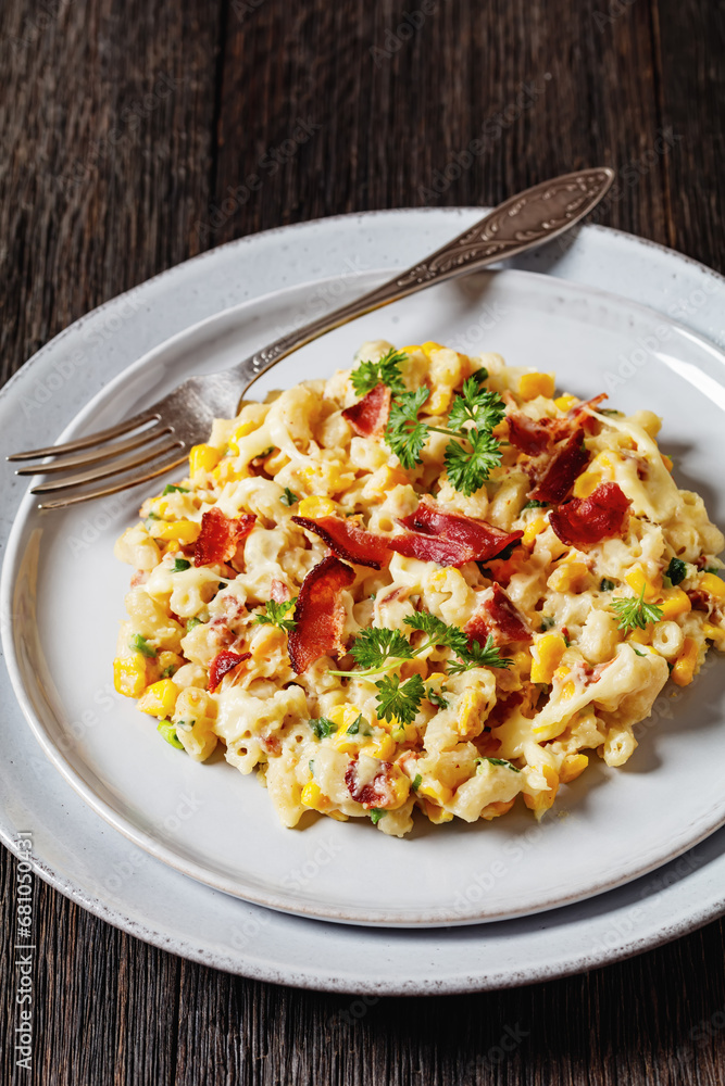 macaroni and cheese with corn, bacon topped with panko breadcrumbs on plates with fork on dark wooden table, vertical view, close-up macaroni and cheese with corn, bacon topped with panko breadcrumbs on plates with fork on dark wooden table, vertical view, close-up