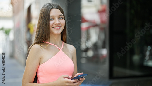 Young beautiful girl using smartphone smiling at street