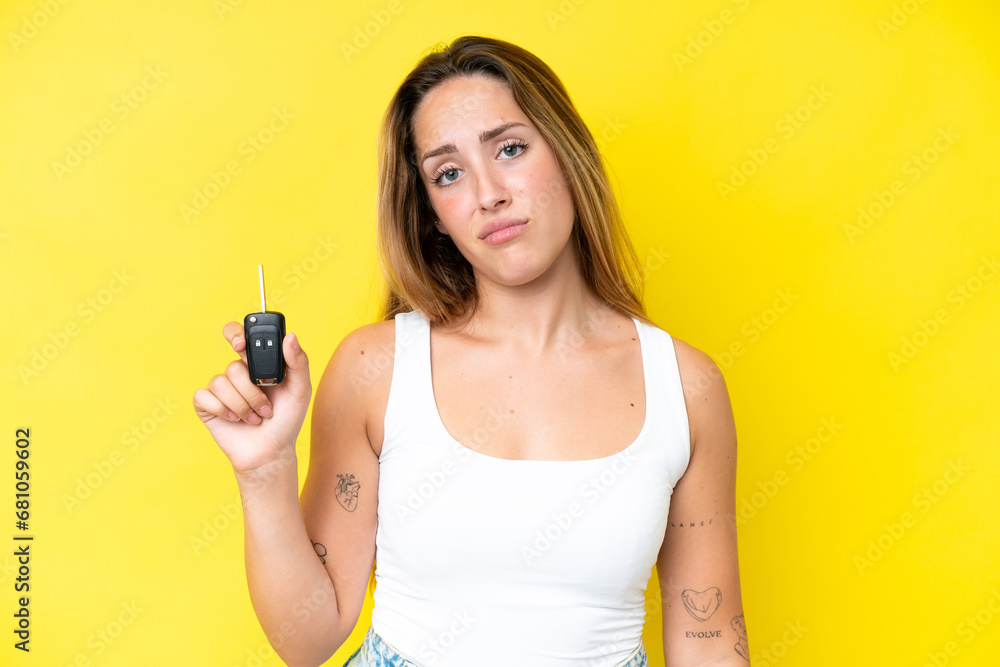 Young caucasian woman holding car keys isolated on yellow background with sad expression Young caucasian woman holding car keys isolated on yellow background with sad expression