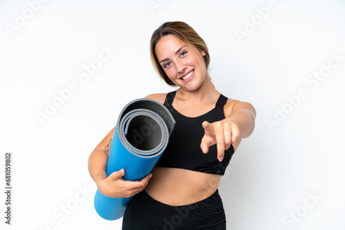 Young caucasian woman going to yoga classes while holding a mat isolated on white background pointing front with happy expression © luismolinero