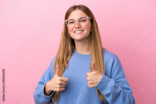 Young blonde woman isolated on pink background With glasses and with thumb up