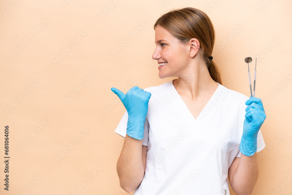 Dentist caucasian woman holding tools isolated on beige background pointing to the side to present a product