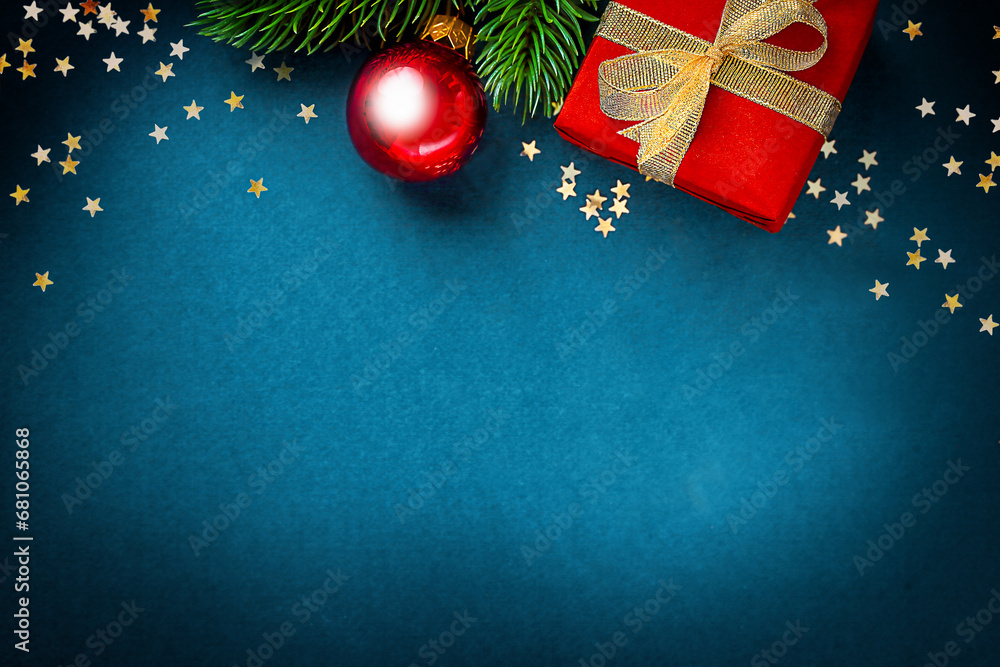 one gift box wrapped in red paper and tied with a golden bow, a sprig of a Christmas tree with a toy on a blue background, with golden confetti in the shape of stars scattered around.