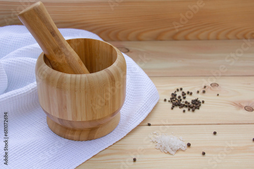 wooden mortar for grinding dried spices, pepper and others, next to pepper, salt, on a wooden table on a white cloth close-up